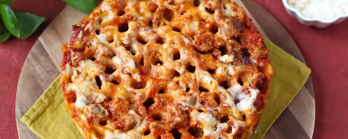 Uunissa paistettu rigatoni-timballo, jossa on makkaraa, besciamellaa ja mozzarellaa