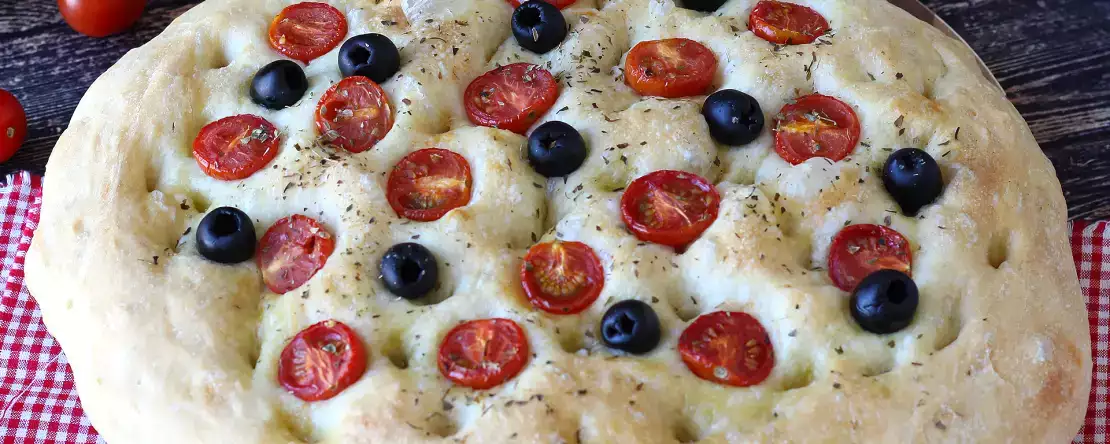 Paksu ja pehmeä focaccia, jossa on kirsikkatomaatteja, oliiveja ja oreganoa